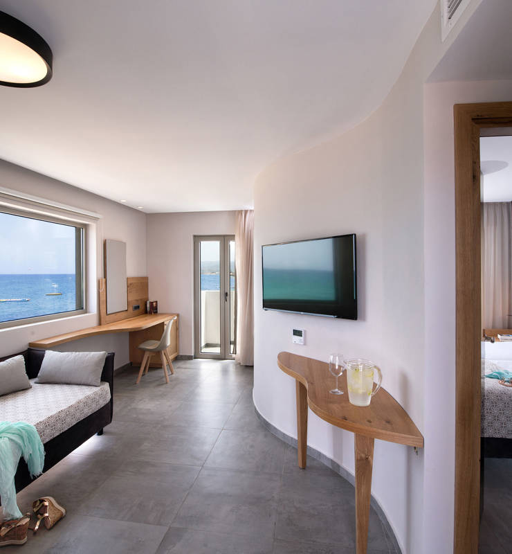 Cactus bay hotel suite living room with a double bed, a TV and a balcony overlooking the sea